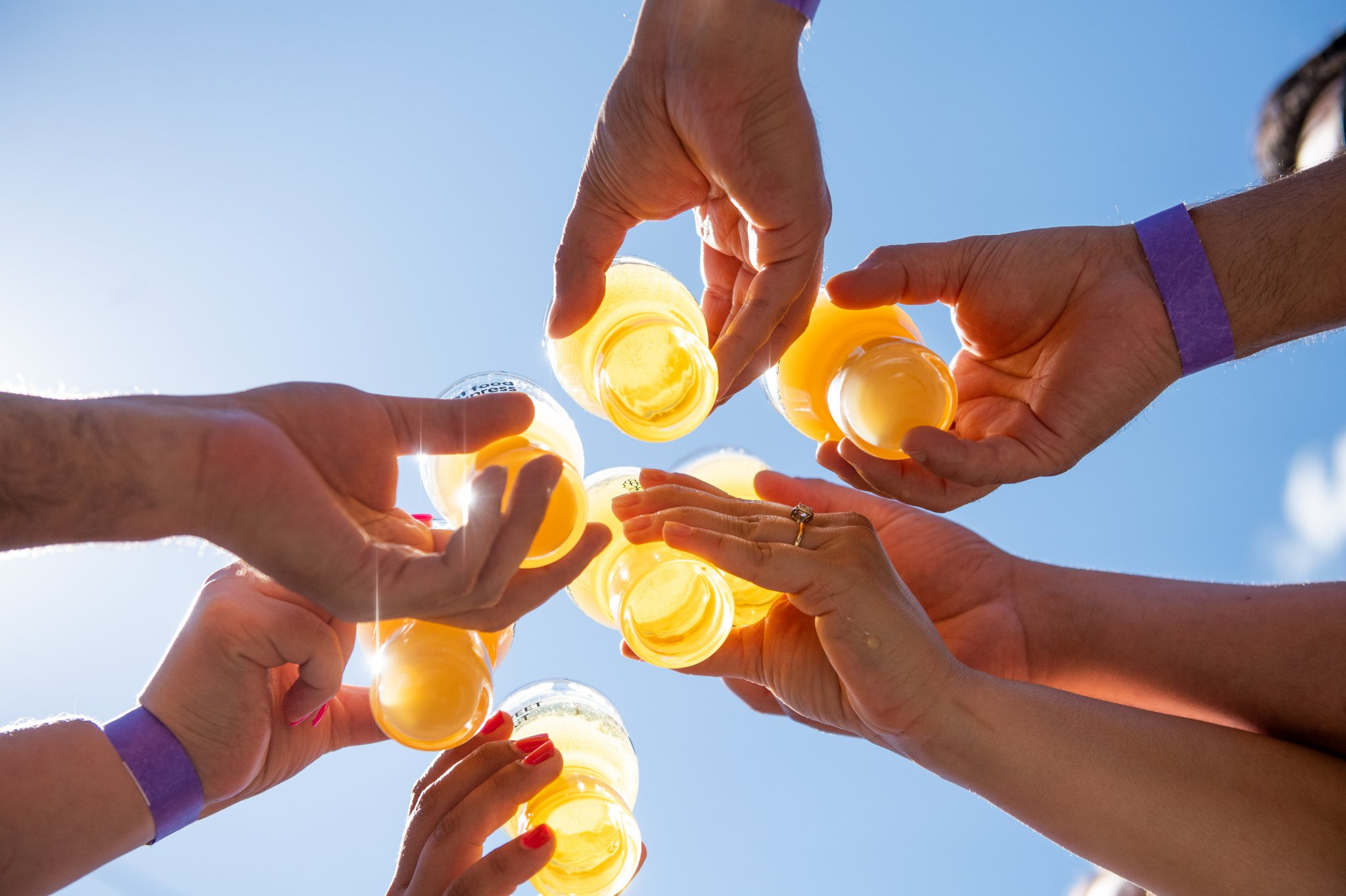 six hands holding beer in glasses cheers with blue sky above