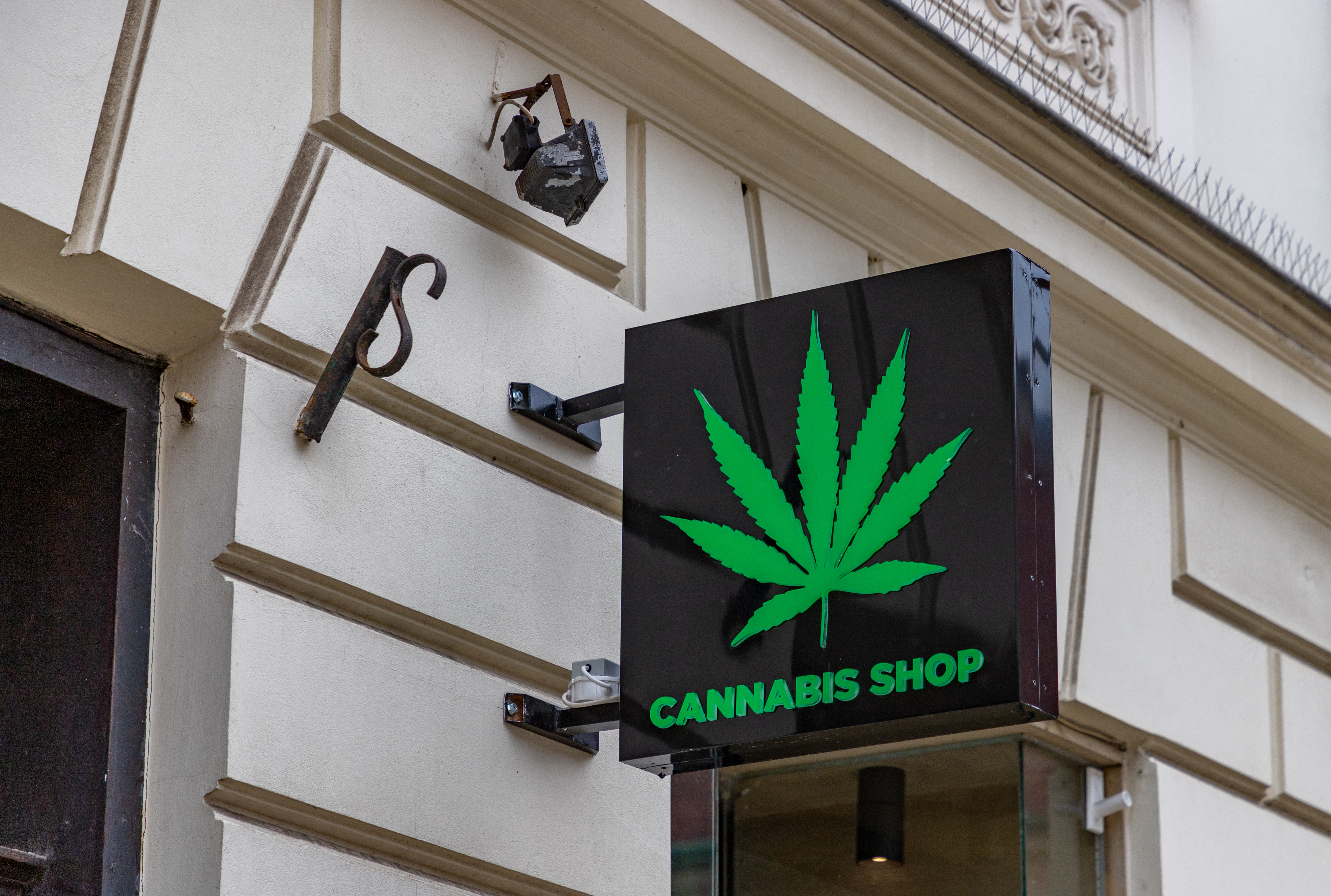 sign on white building: Cannabis Shop in green lettering with a green cannabis leaf with a black background