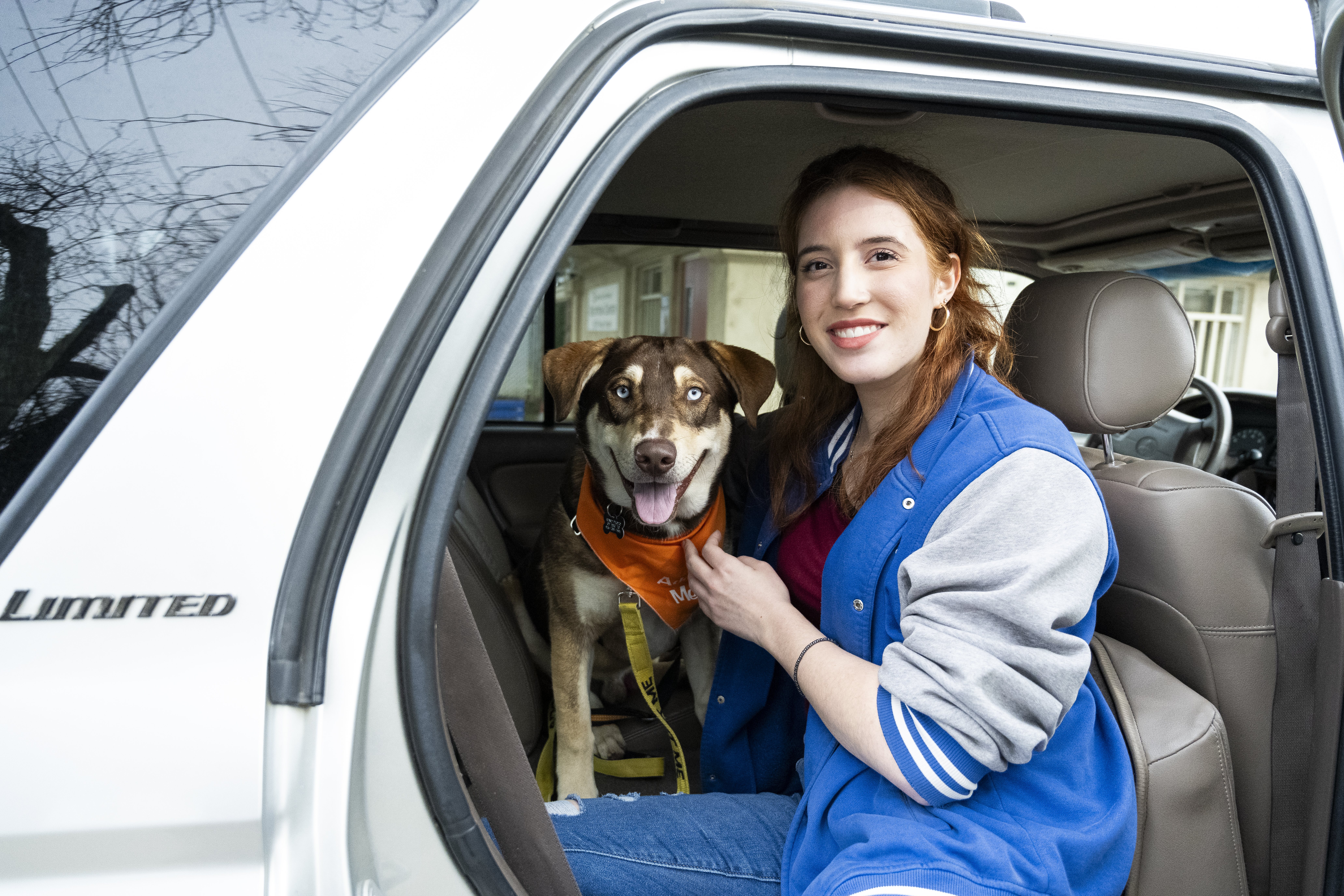 Woman with brown hair and a blue jacket sitting in a car with a medium sized dog