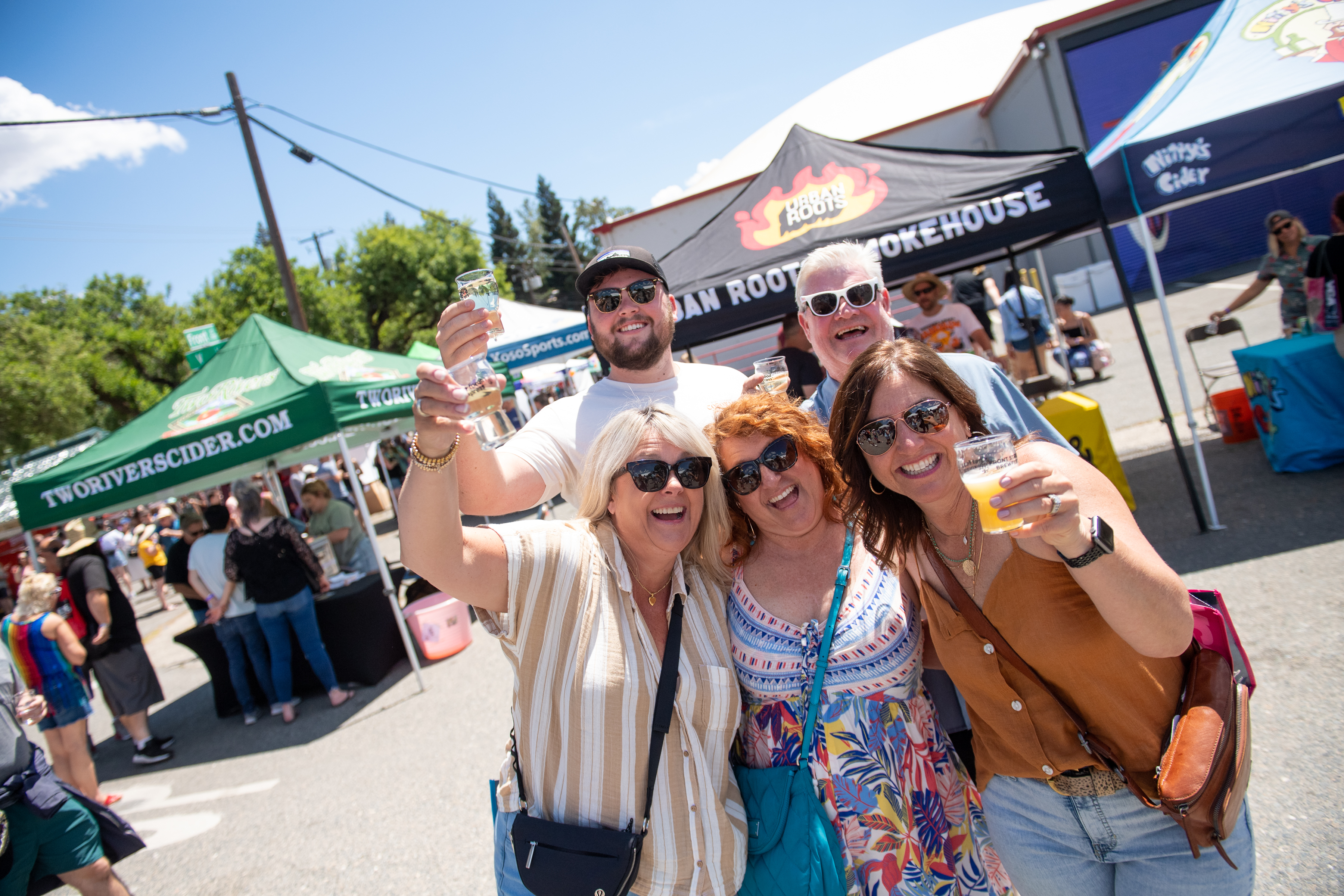 five people gathered for a photo at the brewfest, three holding up glasses of beer.